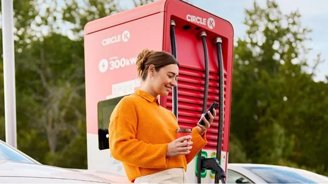 Billede af kvinde med mobil, der oplader sin bil